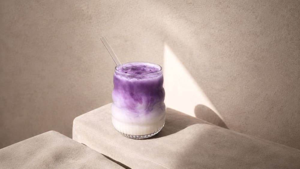 Ube latte glacé à la couleur violette naturelle servi dans un verre transparent sur fond beige minimaliste